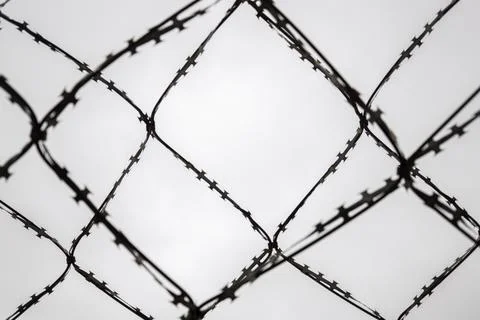 Close-up abstract view of razor wire fence against a bright, overcast sky Stock Photos