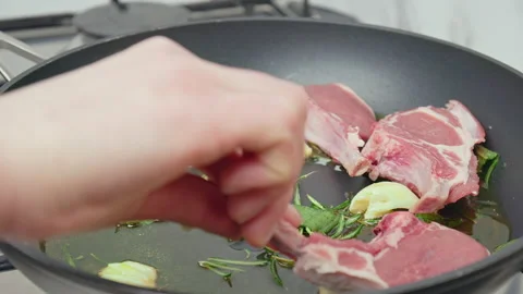 Close-up adding raw lamb ribs cutlets in a frying pan with greens in 4K. Stock Footage 145999340