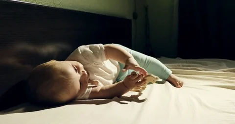 Close-up of adorable curious baby playing with wooden toy in the bed. Little Видео 108560686