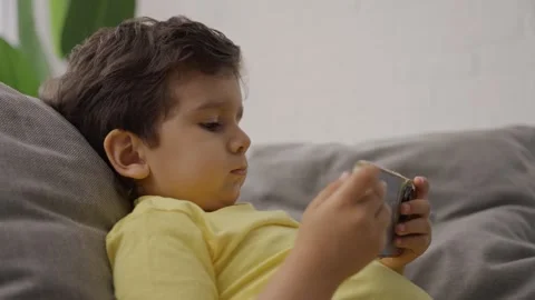 Close up adorable small child sitting on couch playing online games Stock Footage 245591683