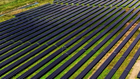 Close aerial shot of long parallel solar panel rows stretching across a green Video stock 325056511