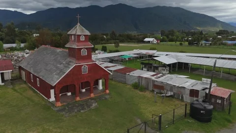 Close Aerial View of Old Red Wooden Church with Mountains and Heavy Clouds in Le Stock Footage 325335539