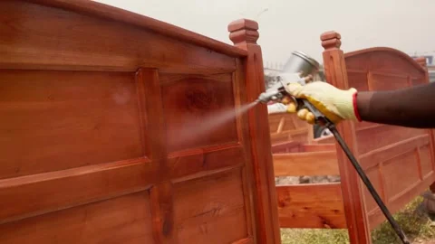 Close-up of African carpenter using spray gun to varnish wooden bed frame Stock Footage 346733952