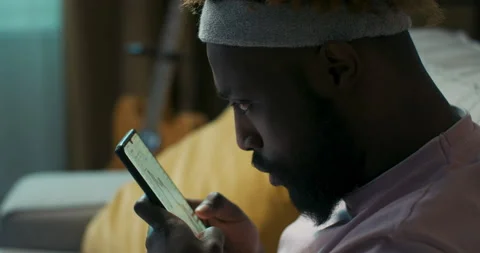 Close-up of African-looking guy holding phone and checking financial charts. The 스톡 동영상 218113053