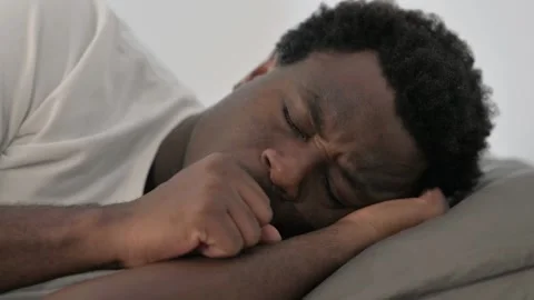 Close up of African Man Coughing while Lying on Side in Bed Video stock 299757502