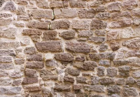 Close-up of an aged masonry wall with uneven stone blocks and worn natural te Stock Photos