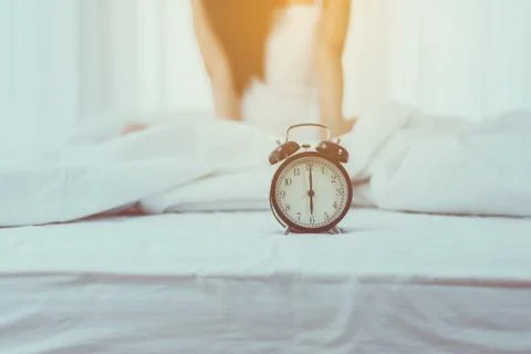 Close up of alarm clock at 6 o'clock in the morning and blurred woman waking Stock Photos