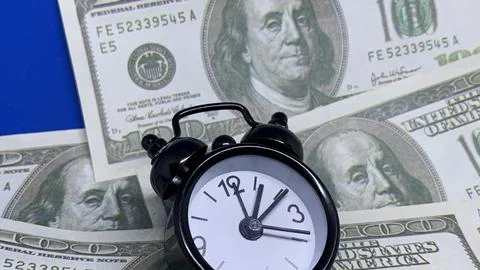 Close-up of an alarm clock surrounded by one-hundred-dollar banknotes, Stock Photos