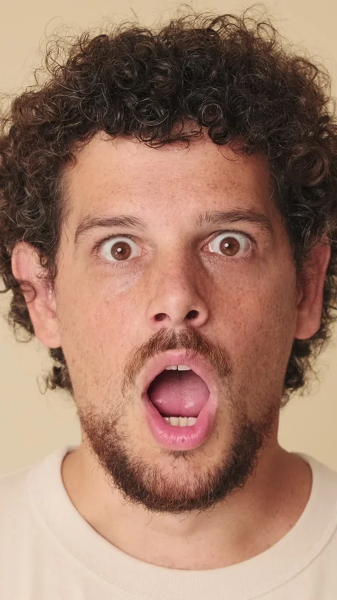 Close-up of amazed man looking at camera expressing wow in studio on beige Vídeo Stock 252501999