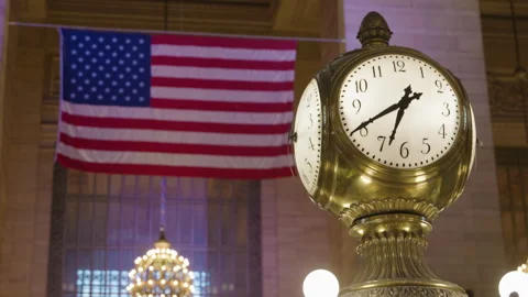 Close up of American flag with clock in foreground at Grand Central terminal Stock Footage 345626446