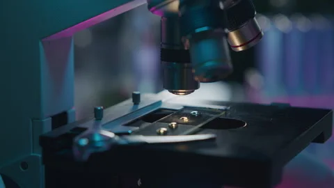 Close Up of Analyzing Specimen on Illuminated Slide under Microscope Stock Footage 315130822