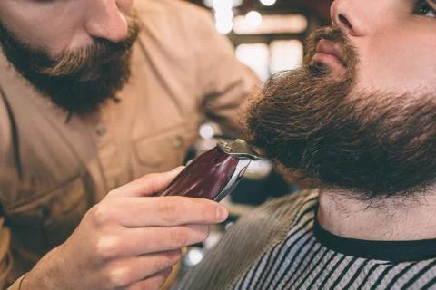 Close up and cut view of a guy that is cutting some beard of his customer with 库存照片