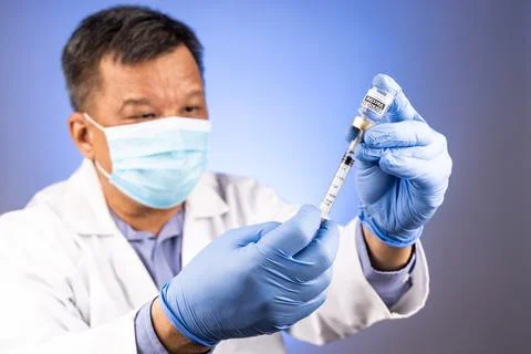 Close-up and focus on syringe inserted into Covid-19 vaccine vial by Asian Stock Photos