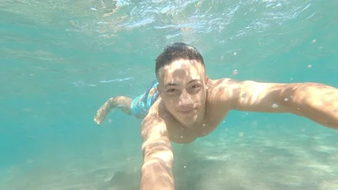 Close up and portrait of young man holding a camera and swimming underwater in t Stock Footage 143362802