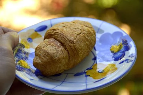 Close up and selective focus of hand holding croissant on a small plate. Stock Photos