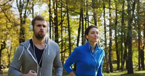 Close up and slow motion of young sporty couple in headphones jogging in the Stock Footage 82504045