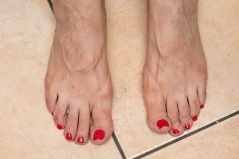 A close-up and top view on the bare feet of an older lady, with painted red t 스톡 사진