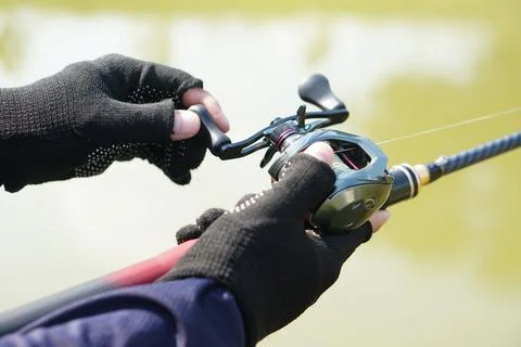 Close-up of angler hands using a baitcasting reel and fishing rod outdoors on a  Fotos Stock