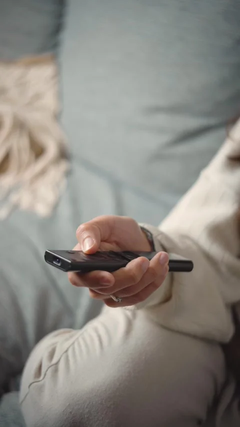Close-up of an anonymous woman's hand using a TV remote at home, representing en Stock Footage 346162397
