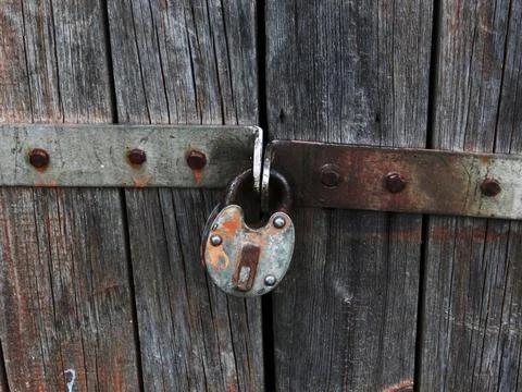 Close-up of an antique rusted padlock locking a worn wooden door Stock Photos