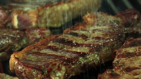 Close up of appetizing meat steak being seasoned with coarse salt on a hot ba Stock Footage 127715384