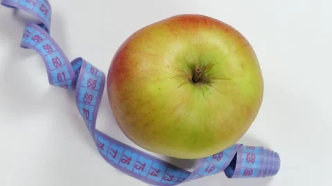 Close-up of an apple and measuring tape slowly rotating on a white background. Stock Footage 310655889