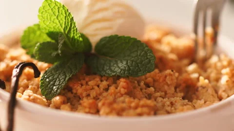 Close up of an apple crumble with vanilla ice cream is taken with a dessert on a Stock Footage 128587740