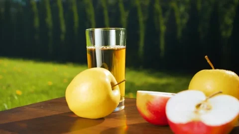 Close-up of an apple rolling on a wooden table towards a glass of apple juice. Stock-Footage 275069923