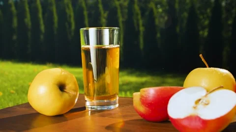 Close-up of an apple rolling on a wooden table towards a glass of apple juice. Video stock 275070076