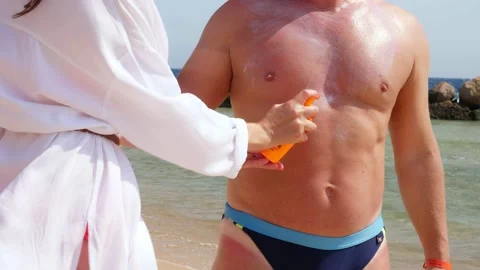 Close-up, applying sunscreen or spray lotion to man skin . on beach, under hot Stock Footage 136740434