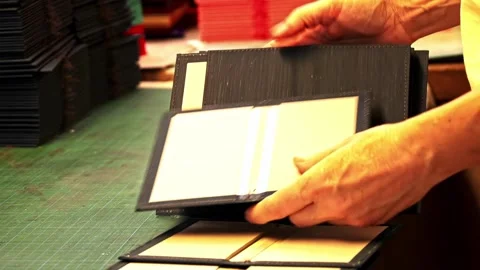 Close up of artisan hands making black leather book covers in workshop Stock Footage 332431112