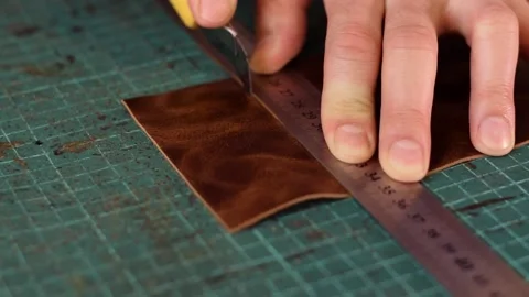 Close up of artisan's hands measuring and cutting leather with knife. Stock Footage 150477627
