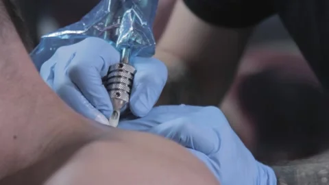 Close-up of artist in blue gloves doing tattoo on back of person with short hair Stock Footage 148676946