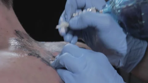 Close-up of artist in blue gloves doing tattoo on back of person with short hair Stock Footage 148676973