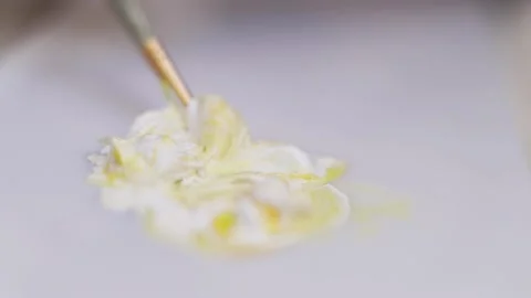 Close-up of artist using a brush to mix paint colors white and yellow Stock Footage 140037817