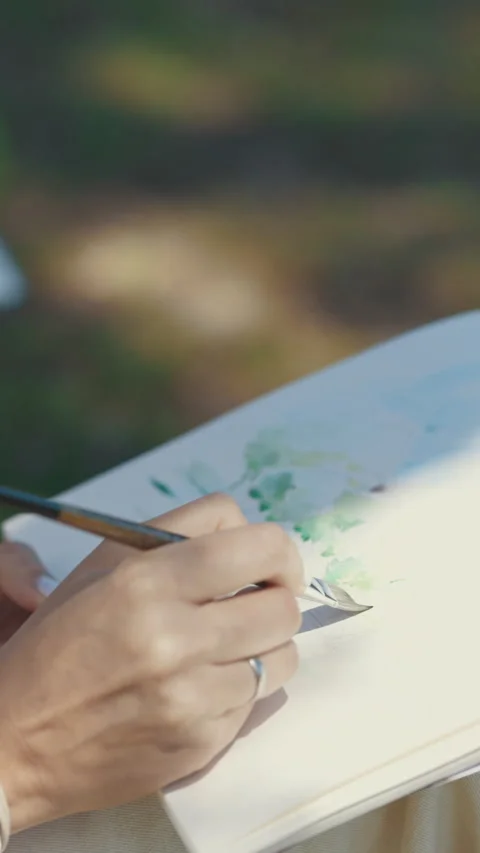 Close-up of the artists hand and sheet of album painting a watercolor landscape Stock Footage 328645006