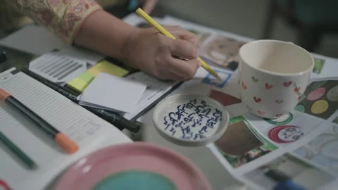 Close up of artist's hand designing and coloring a ceramic mug and plate using Stock Footage 309752327