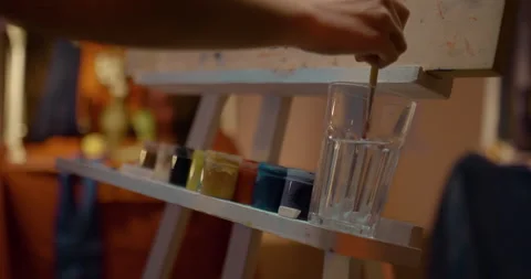 Close-up, the artist's hand dissolves red paint in water, soaks a brush into a Stock Footage 167973983