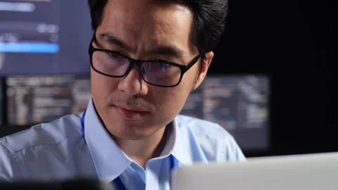 Close Up Of Asian Male Programmer Looking At Tablet And Writing Code By A Laptop Stock Footage 230181935
