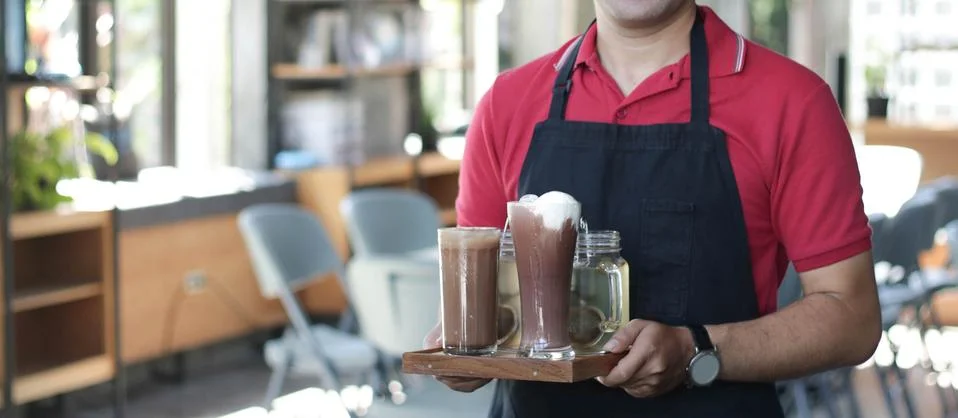 Close up asian man barista smiling holding tray with coffee on it and cafe Stock Photos