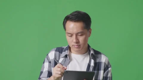 Close Up Of Asian Man Taking Note On Tablet While Walking On Green Screen Stock Footage 248006566