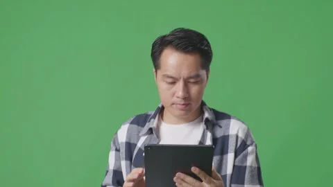 Close Up Of Asian Man Using Tablet While Walking On Green Screen In The Studio Stock Footage 248006536