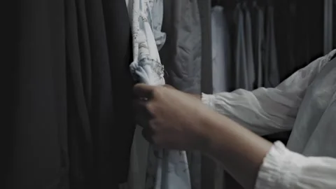 Close-up of an Asian woman's hands browsing through rack of clothes in closet Video stock 299787176