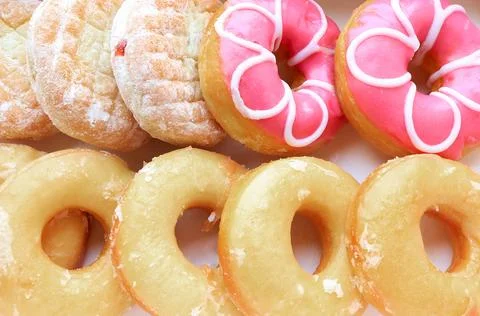 Close up of assorted glazed sweet donuts in a paper box on a table. Stock Photos