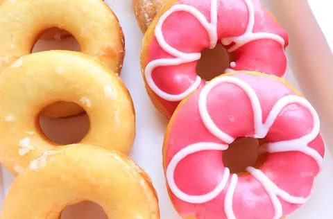 Close up of assorted glazed sweet donuts in a paper box on a table. Stock Photos