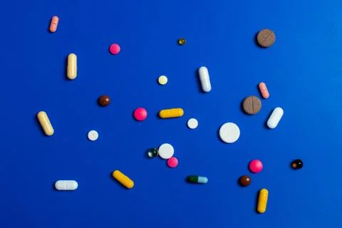 Close-up of assorted multi-colored pills on a blue background. Medical flat l Stock Photos