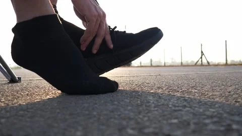Close-up of athlete putting on black running shoes on asphalt road at sunrise Video stock 329355021
