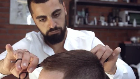 Close-up attentive handsome young man barber with a beard gently cuts the hair Stock Footage 112337210
