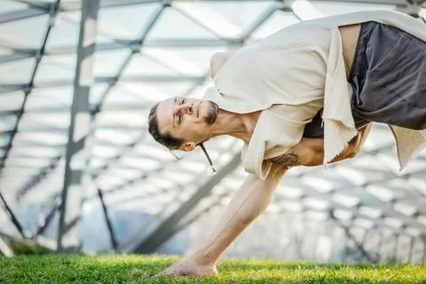 Close up of attractive athletic man practicing yoga and warming up outdoors. Stock Photos