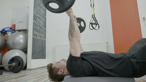 Close up of an attractive beautiful man lifting up weights in a gym while lyi Stock Footage 87202910
